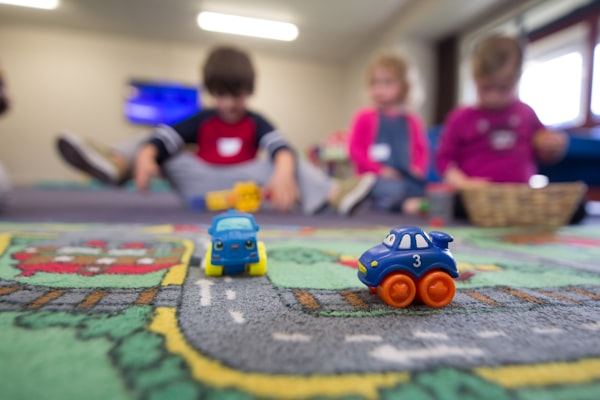 Children playing with toy cars on a road-themed rug at Mini Minds.